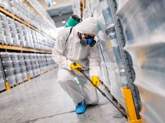 Exterminator in factory spraying pesticide with sprayer.